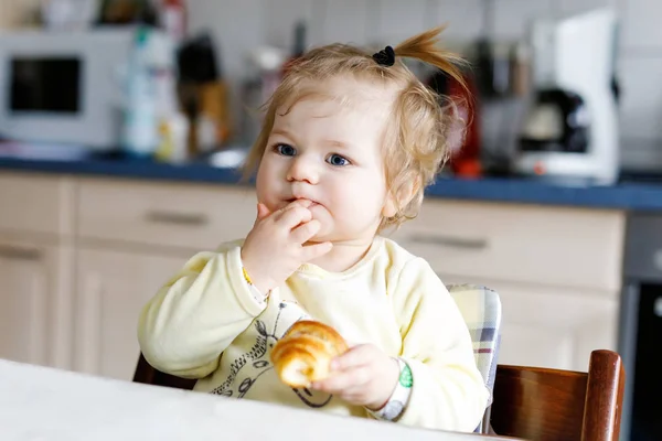 Küçük mutlu kız bebek kahvaltıda ya da öğle yemeğinde taze kruvasan yiyor. Çocuklar için sağlıklı beslenme — Stok fotoğraf