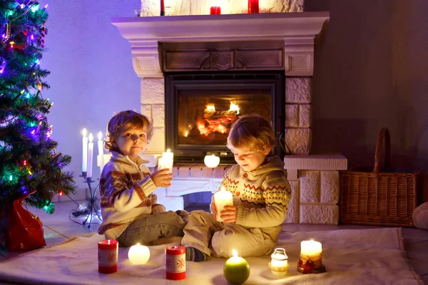 Cute toddler boys, blond twins playing together and lookinig on fire in chimney. Family celebrating xmas holiday
