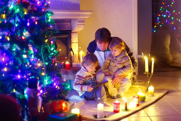 Baba ve Noel arifesi zamanında şömine baca tarafından oturan iki küçük çocuğu. — Stok fotoğraf