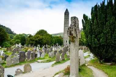 Taş yuvarlak kule ve bir manastır yerleşim bazı kalıntıları aslında Glendalough vadisinde 6 yüzyılda inşa, County Wicklow, İrlanda güneşli bir günde