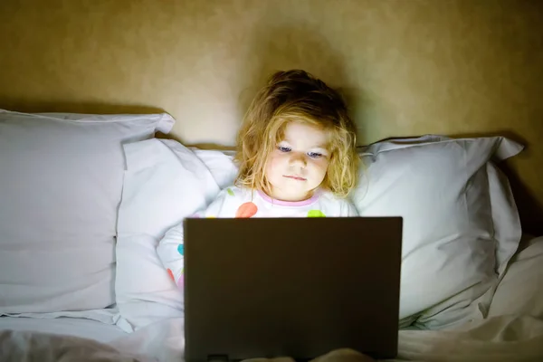 Söt bedårande litet småbarn flicka tittar karikatyrer på laptop i sängen. Trött bebis barn med Tablet-enhet med touch-teknik. — Stockfoto