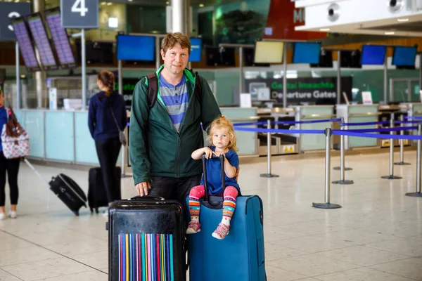 Linda niñita y padre en el aeropuerto. Familia feliz viajando en avión, haciendo vacaciones. Joven padre e hija con maletas esperando el vuelo. Familia en viaje — Foto de Stock