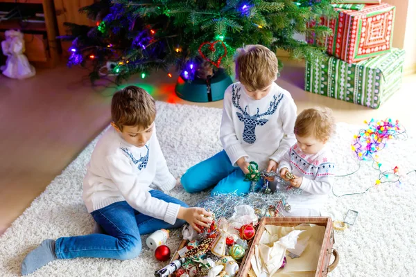 Two little kid boys and adorable baby girl decorating Christmas tree with old vintage toys and balls. — Stock Photo, Image