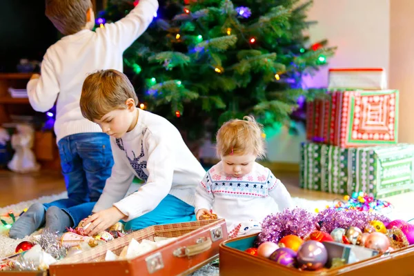 Dos niños y una adorable niña decorando el árbol de Navidad con viejos juguetes y pelotas vintage . —  Fotos de Stock