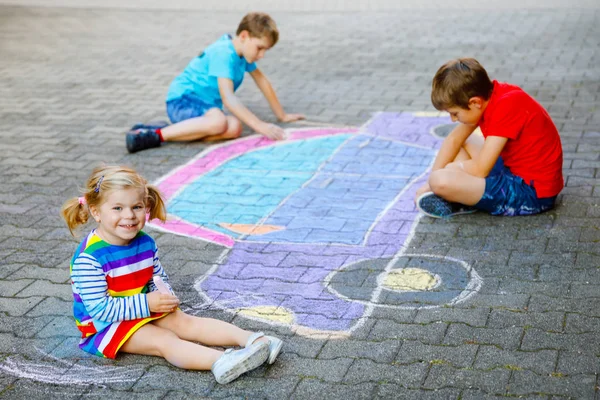 3人の小さな子供、2人の学校の男の子と幼児の女の子は、アスファルトにカラフルなチョークで車の絵の描画を楽しんでいます。一緒に遊んで地面に絵を描く兄弟。クリエイティブなレジャー — ストック写真