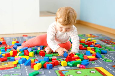 Eğitici oyuncaklarla oynayan sevimli bir kız bebek. Mutlu sağlıklı bir çocuk, evdeki renkli tahta bloklarla eğleniyor. Bebek öğrenme renkleri ve biçimleri