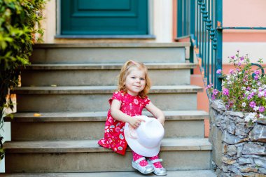 Pembe elbiseli, moda elbiseli, diz altı çoraplı ve şapkalı güzel küçük bir kız çocuğunun portresi. Renkli evin önünde poz veren mutlu sağlıklı bebek..