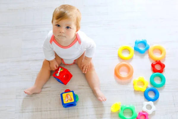 Schattig babymeisje spelen met de educatief speelgoed in de kinderkamer. Gelukkig gezond kind plezier met kleurrijke verschillende speelgoed thuis. Kind proberen kunststof piramide te bouwen en het gebruik van blokken met letters — Stockfoto