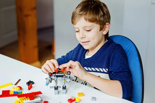 Criança loira brincando com muitos blocos de plástico coloridos. Menino da escola bonito se divertindo com a construção e criação de robô. Lazer criativo moderno técnico e robótico . — Fotografia de Stock