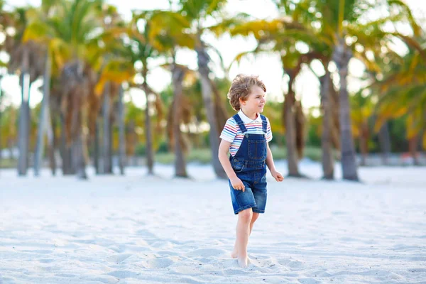 Adorable active little kid boy having fun on tropical beach of island. Happy cute child relaxing, playing, enjoying, running and jumping on sunny warm day near palms and ocean. Active family vacations — Stock Photo, Image