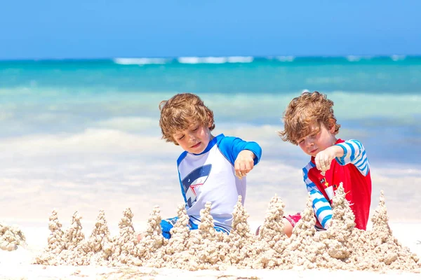 Twee kleine jongens die plezier hebben met het bouwen van een zandkasteel op tropisch strand op het eiland. Gezonde kinderen die samen spelen tijdens hun vakantie. Tweelingen, gelukkige broers lachen en glimlachen — Stockfoto