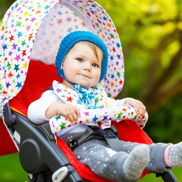 可爱的漂亮的小女孩，戴着蓝色的温暖的帽子坐在婴儿车或婴儿车里等妈妈。蓝眼睛的快乐微笑的孩子。小女儿和家人一起出去散散步 — 图库照片