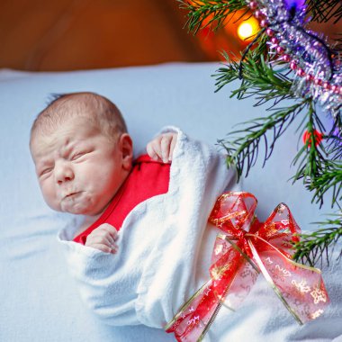 Bir hafta önce yeni doğan bebek battaniye arka plan üzerinde renkli garland ışıkları ile Noel ağacı yakınındaki sarılı. Portre sevimli çocuk, küçük bebek kameraya bakıyor. Aile, Xmas, doğum, yeni hayat.