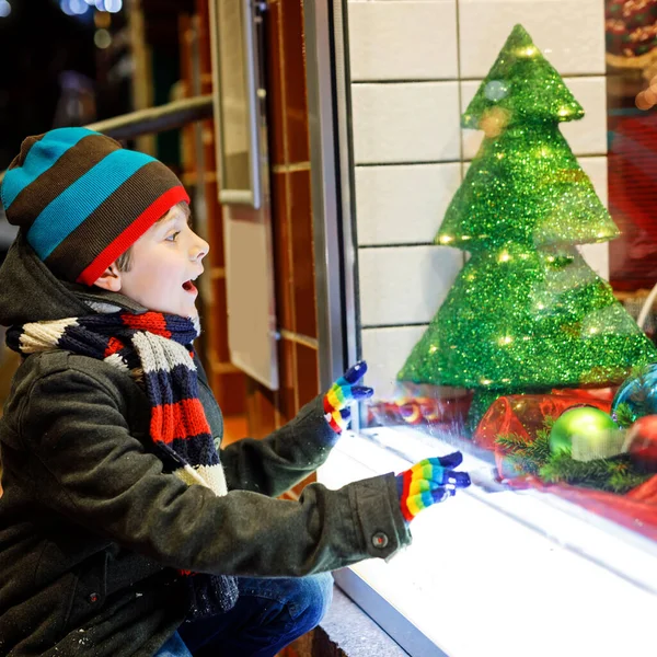 Noel pazarı üzerinde şirin küçük okullu çocuk çocuk. Komik mutlu çocuk moda kış giysileri pencere alışveriş yapma hediyeler, xmas ağacı ile dekore edilmiştir. Bayramlar, yılbaşı, çocukluk ve insanlar kavramı — Stok fotoğraf