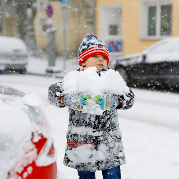 Rolig liten pojke i färgglada kläder spelar utomhus under starkt snöfall. Aktiv fritid med barn på vintern på kalla snöiga dagar. Glada barn som har roligt, leker med snö. Vintermode. — Stockfoto