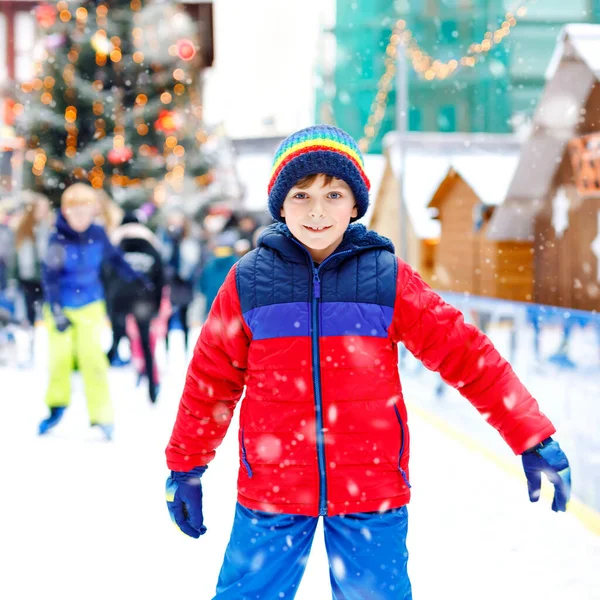 快乐的小男孩穿着五颜六色的保暖衣服在圣诞市场或集市的溜冰场上溜冰。健康的孩子在滑冰上玩得很开心.很多人庆祝节日，并有积极的寒假 — 图库照片