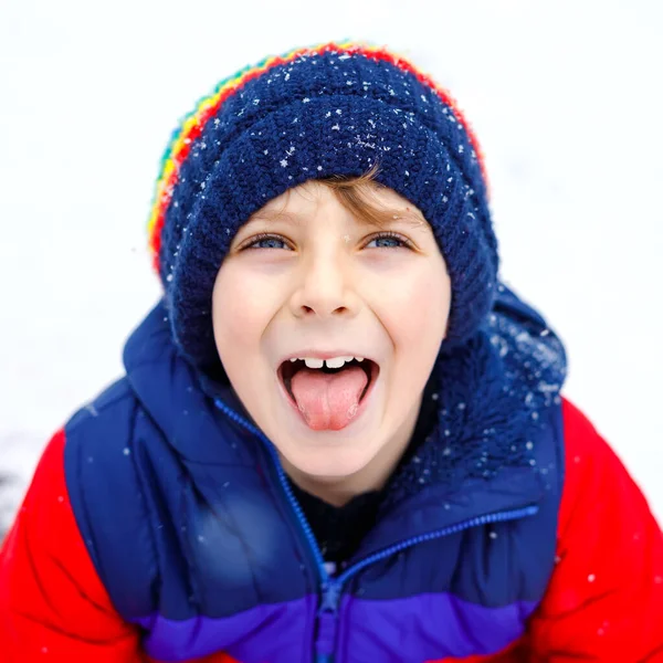 Porträt eines kleinen Schuljungen in bunten Kleidern, der bei Schneefall im Freien spielt. Aktive Freizeitgestaltung mit Kindern im Winter an kalten Schneetagen. Glückliches gesundes Kind, das Spaß hat und mit Schnee spielt. — Stockfoto