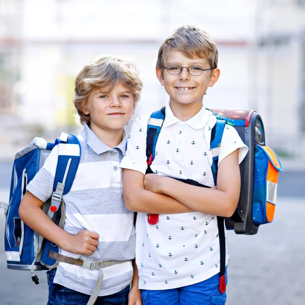 Dois rapazinhos com mochila ou mochila. Miúdos da escola a caminho da escola. Crianças saudáveis adoráveis, irmãos e melhores amigos ao ar livre na rua saindo de casa. De volta à escola. Irmãos felizes.. — Fotografia de Stock