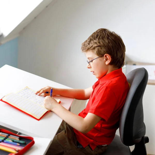 Ragazzino carino con gli occhiali a casa a fare i compiti, scrivere lettere con penne colorate. Un bambino che fa esercizio, in casa. Scuola elementare e l'istruzione, immaginare il concetto di fantasia.. — Foto Stock