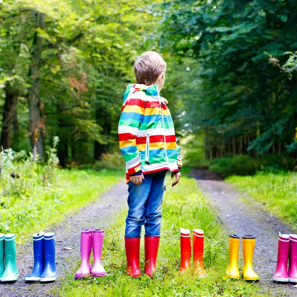 Little kid boy and group of colorful rain boots. Blond child standing in autumn forest. Close-up of schoolkid and different rubber boots. Footwear and fashion for rainy fall — Stock Photo, Image