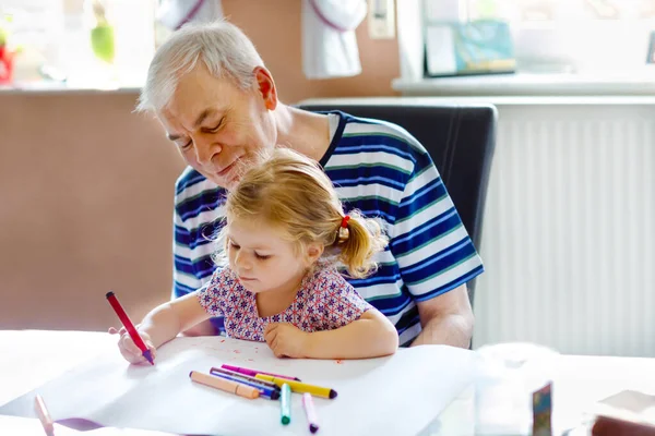 Carino bambino bambina e bel nonno anziano pittura con matite colorate a casa. Nipote e uomo si divertono insieme — Foto Stock