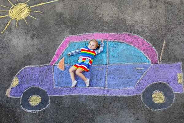 Adorabile bambina che gioca con gessetti colorati e dipinge grande immagine auto su asfalto. Bambino felice che gioca fuori. Tempo libero creativo per bambini all'aperto in estate — Foto Stock