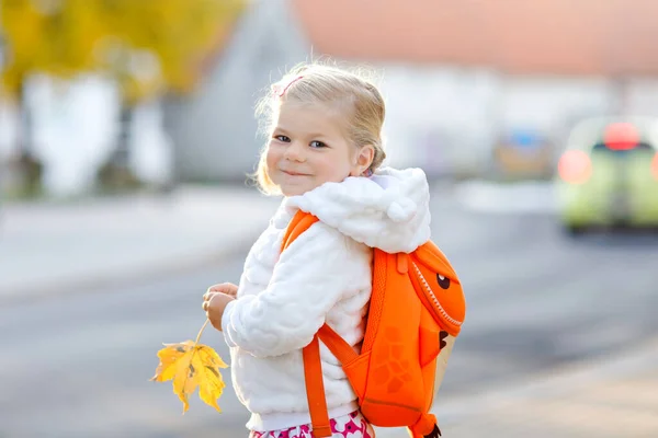 Linda niñita adorable en su primer día yendo a la escuela de juegos. Bebé feliz y saludable caminando a la guardería. niño con mochila que va a la guardería en la calle de la ciudad, al aire libre —  Fotos de Stock