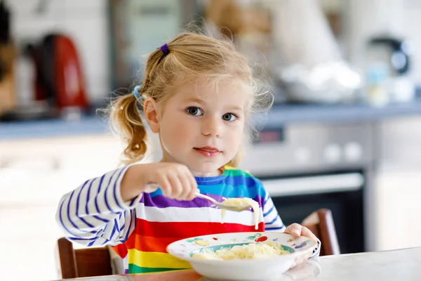 Adorable toddler girl eating healthy chicken noodle soup for lunch. Cute happy baby child taking food at home or nursery daycare or kindergarten and learning using spoon. — Stockfoto