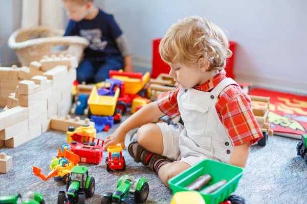 Pequeno menino da criança bonito brincando com brinquedos de carro e trator. Criança feliz brincando em playschool ou jardim de infância. crianças em creche fazendo atividade — Fotografia de Stock