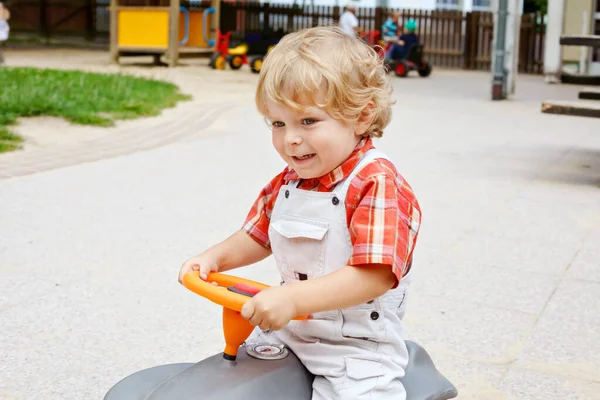 Little cute toddler boy playing with car and tractor toys outdoors. Happy baby child playing at playschool or kindergarten. children at day care doing activity — Stock Photo, Image