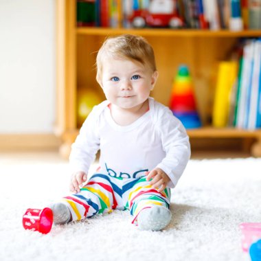 Bebek odasında eğitici oyuncaklarla oynayan sevimli bir kız. Mutlu sağlıklı çocuk evde renkli farklı oyuncaklarla eğleniyor. Bebek gelişimi ve ilk adımlar, çalmayı ve yakalamayı öğrenmek..