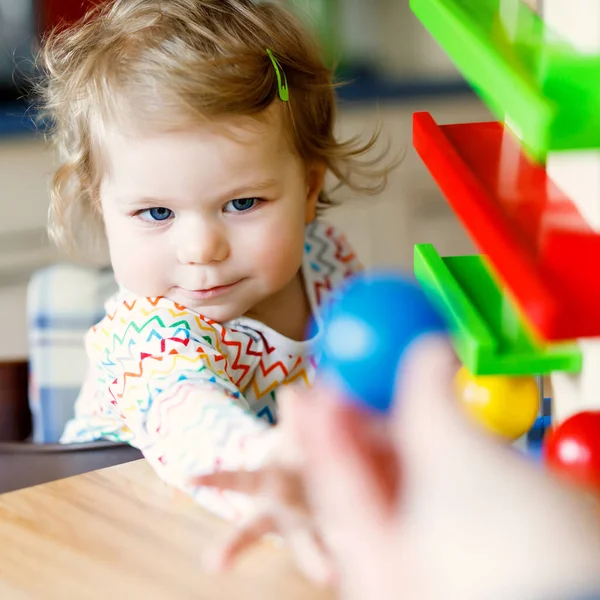 Адекватная симпатичная маленькая девочка, играющая с развивающими игрушками дома или в детском саду. Счастливый здоровый ребенок веселится с разноцветными деревянными игрушечными шариками. Ребенок учится держать и катить мяч . — стоковое фото