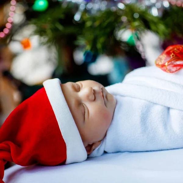 Mooie een week oude pasgeboren baby verpakt in deken in de buurt van kerstboom met kleurrijke slinger lichten op de achtergrond. Een close-up van een schattig kind dat vredig slaapt. Familie, Kerstmis, geboorte, nieuw leven. — Stockfoto