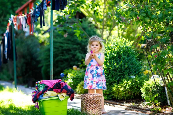 Adorable niña colgando ropa para secar en el jardín después de hacer la ropa. Feliz niño ayudando en el hogar. Familia trabajando juntos, niño aprendiendo a ayudar . —  Fotos de Stock