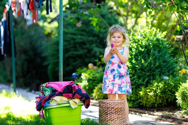 Entzückendes kleines Mädchen, das Kleidung zum Trocknen im Garten aufhängt, nachdem es Wäsche gewaschen hat. Glückliches Kind, das im Haushalt hilft. Familie arbeitet zusammen, Kind lernt zu helfen. — Stockfoto