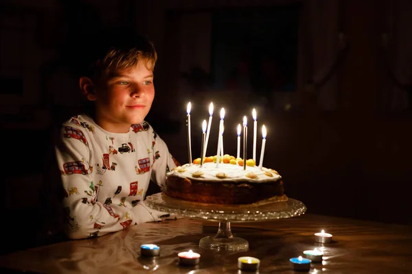 Adorabile bambino biondo felice che festeggia il suo compleanno. Bambino che soffia candele sulla torta al forno fatta in casa, al coperto. Festa di compleanno per i bambini delle scuole, festa di famiglia — Foto Stock