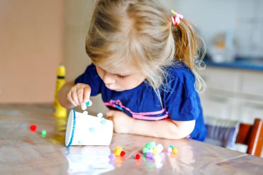 Küçük kız karantina hastalığı sırasında kağıt bardaklardan, renkli ponponlardan ve yapıştırıcıdan el feneri yapıyor. Mutlu yaratıcı çocuk, evde eğitim ve ebeveynlerle evde bakım.