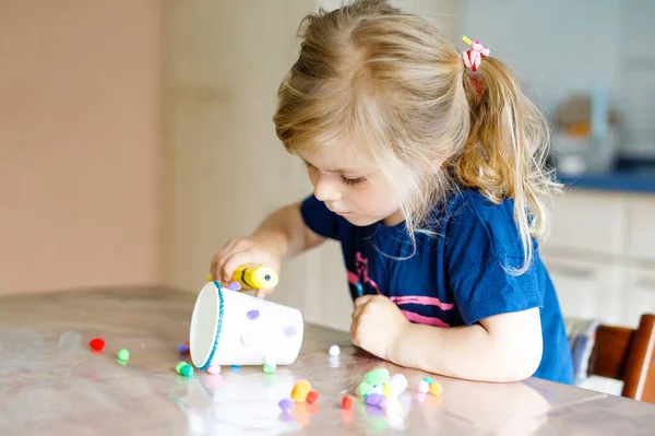 Piccola bambina che fa lanterna artigianale con bicchieri di carta, pompon colorati e colla durante la pandemia coronavirus malattia da quarantena. Felice bambino creativo, scuola materna e assistenza domiciliare con i genitori — Foto Stock