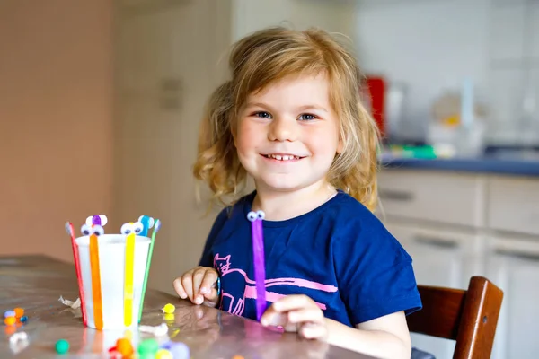Маленька дівчинка робить косметичний ліхтар з паперовими чашками, барвистими помпонами та клеєм під час пандемії коронавірусної хвороби. Щаслива творча дитина, домашнє господарство та догляд за домом з батьками — стокове фото