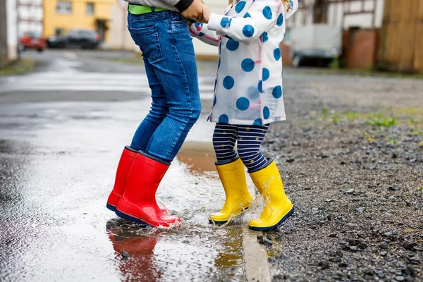 Close-up de duas crianças, menina criança e menino vestindo botas de chuva vermelhas e amarelas, andando durante o trenó. Irmãos felizes, irmão e irmã a saltar para a poça. Divertindo-se ao ar livre, família ativa — Fotografia de Stock