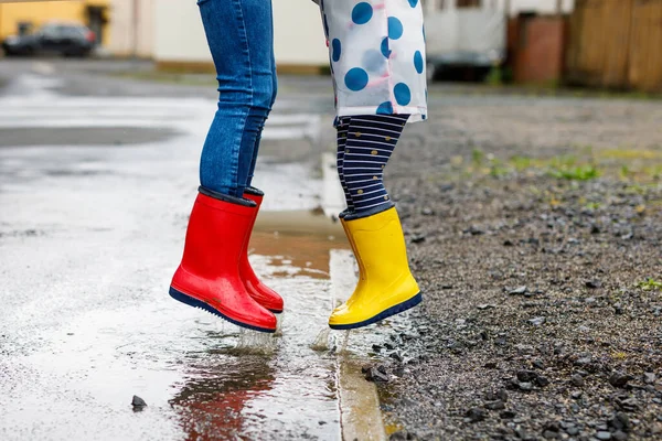 Primer plano de dos niños, niña y niño con botas de lluvia rojas y amarillas, caminando durante el aguanieve. Felices hermanos, hermano y hermana saltando al charco. Divertirse al aire libre, familia activa — Foto de Stock