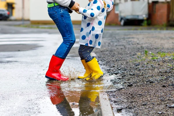 Primer plano de dos niños, niña y niño con botas de lluvia rojas y amarillas, caminando durante el aguanieve. Felices hermanos, hermano y hermana saltando al charco. Divertirse al aire libre, familia activa — Foto de Stock