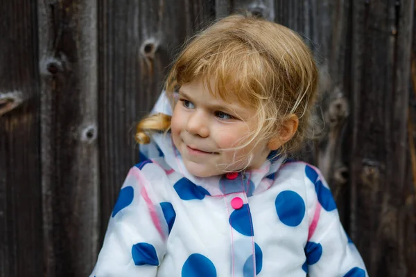 Außenporträt eines glücklich lächelnden kleinen Mädchens mit Regenjacke an einem regnerischen, bewölkten Tag. Nettes gesundes Kind in bunten Kleidern Outdoor-Aktivität — Stockfoto