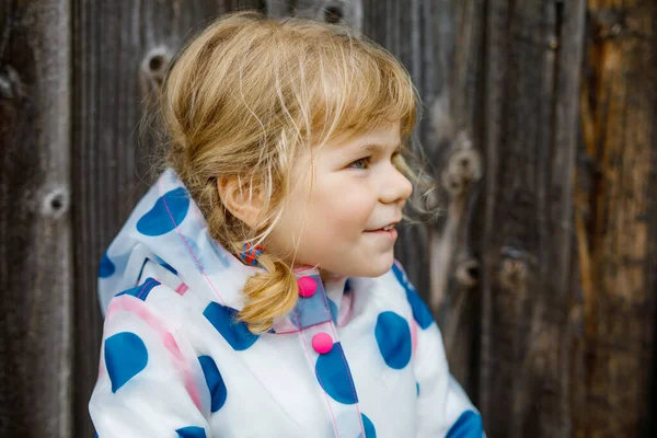 Utomhus porträtt av glada leende liten småbarn flicka bär regnjacka på regnig molnig dag. Söta friska barn i färgglada kläder utomhus aktivitet — Stockfoto