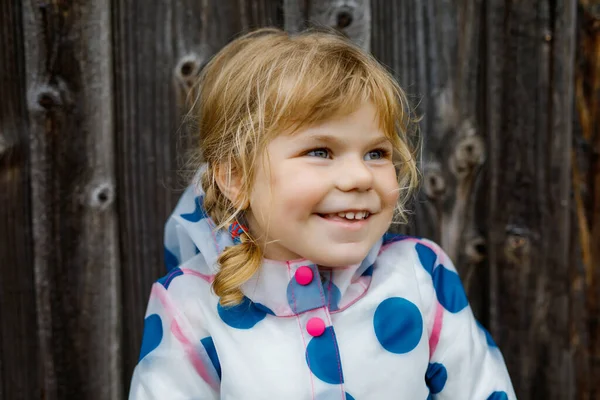 Outdoor portret van vrolijk lachend peutermeisje in regenjas op regenachtige bewolkte dag. Schattig gezond kind in kleurrijke kleding outdoor activiteit — Stockfoto