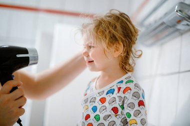 Babam saç kurutma makinesiyle küçük tatlı bir kızın saçlarını yapıyor. Banyo yaptıktan sonra ıslak saçlı sevimli sağlıklı bir bebek. Kızla babanın aile ilişkisi.