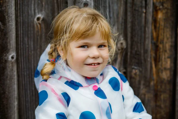 Εξωτερικό πορτρέτο του χαρούμενου χαμογελαστού μικρού κοριτσιού που φοράει αδιάβροχο στις βροχερές συννεφιασμένες μέρες. Χαριτωμένο υγιές παιδί σε πολύχρωμα ρούχα υπαίθρια δραστηριότητα — Φωτογραφία Αρχείου