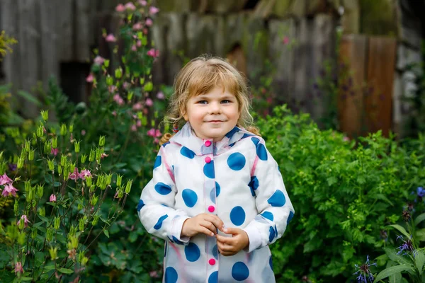 Портрет счастливой улыбающейся маленькой девочки в дождевой куртке в дождливый облачный день. Симпатичный здоровый ребенок в красочной одежде — стоковое фото