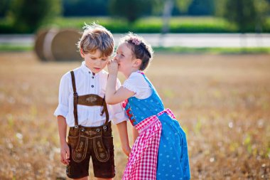 Buğday tarlasında geleneksel Bavyera kostümlü iki çocuk. Alman çocukları Ekim Festivali sırasında saman balyasında oturuyorlar. Almanya 'da yaz aylarında erkek ve kız saman balyalarında oynarlar. En iyi arkadaşlar.