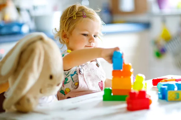 Adorable jeune fille avec lapin en peluche préféré jouer avec des jouets éducatifs en pépinière. Heureux enfant en bonne santé s'amuser avec différents blocs en plastique colorés à la maison. Bébé mignon apprentissage création. — Photo